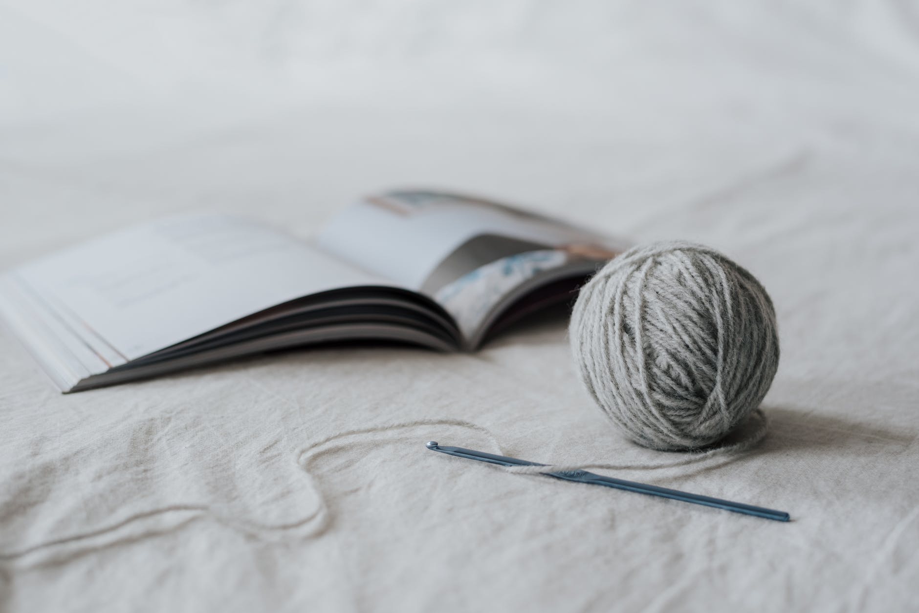 ball of threads and crochet with magazine on white cloth